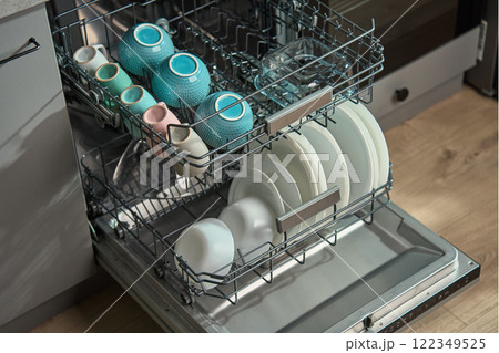 Open dishwasher in kitchen loaded clean crockery items, including white plates, bowls and cups ready for unloading. Modern home appliance 122349525