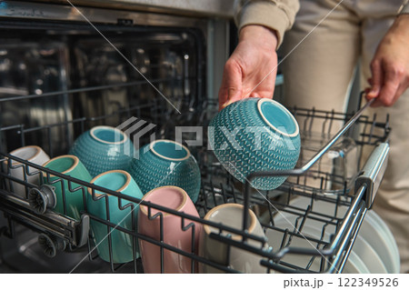 Woman unloading clean dishes and colorful bowl from dishwasher in kitchen. Person performing everyday household chores, using modern home appliance 122349526