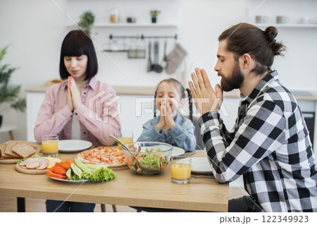 Caucasian family with parents and child praying before breakfast. Focus on togetherness, spirituality, and gratitude over healthy meal. Child around seven years old. Caucasian family with parents and child praying before breakfast. Focus on togetherness, spirituality, and gratitude over healthy meal. Child around seven years old. 122349923