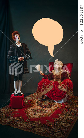 Young man, court servant in red wig standing next to elderly woman, medieval empress and singing to her against dark background with abstract speech bubble 122351187