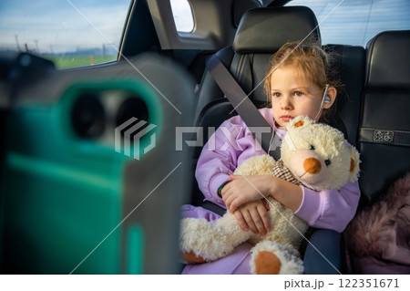 Little girl with teddy bear, tablet and headphones in the car during travel on vacation. Entertainment in the transport for child 122351671