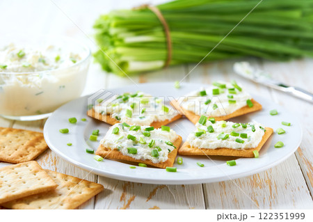 Crispy crackers and a glass bowl with a cream cheese spread and cut chives on a light kitchen table. Crispy crackers and a glass bowl with a cream cheese spread and cut chives on a light kitchen table. 122351999