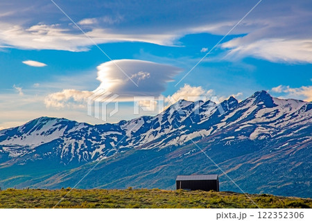 Cabin in front of snow covered mountains and dramatic cloud formations 122352306