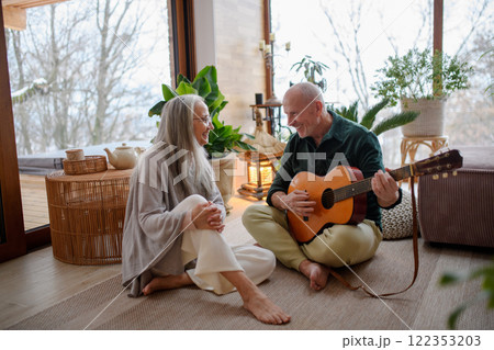 Real older couple at home. Husband playing music on a guitar for his wife. Real older couple at home. Husband playing music on a guitar for his wife. 122353203