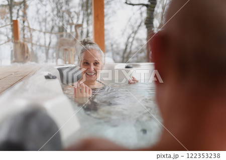 Bathing in hot tub during cold winter day. Older woman sitting in water and talking with husband. Bathing in hot tub during cold winter day. Older woman sitting in water and talking with husband. 122353238
