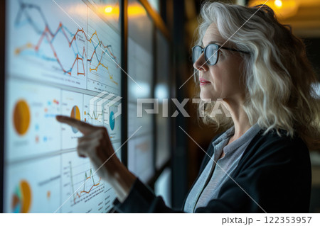 Focused senior female data analyst examines complex data visualizations on a digital screen in a modern office environment 122353957
