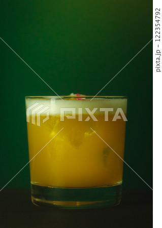 Vibrant Yellow Cocktail with Foam in Lowball Glass Refreshing Drink Against a Lush Green Backdrop 122354792
