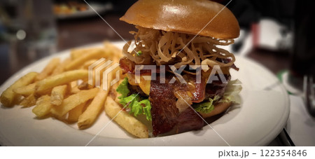 Delectable burger with cheese, bacon, and crispy fried onions, served alongside golden fries, on a grill restaurant's table, emphasizing the meal's presentation and appetizing appeal 122354846