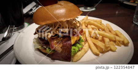 Delectable burger with cheese, bacon, and crispy fried onions, served alongside golden fries, on a grill restaurant's table, emphasizing the meal's presentation and appetizing appeal 122354847