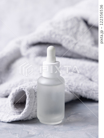 Clear glass dropper bottle with pipette near light grey bath towel closeup, cosmetic mockup Clear glass dropper bottle with pipette near light grey bath towel closeup, cosmetic mockup 122356536