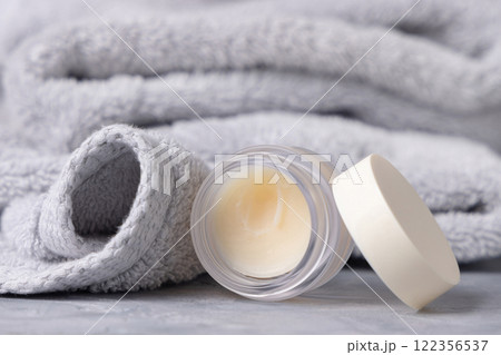 Opened lip balm jar with a blank lid near light gray bath towel closeup, cosmetic mockup 122356537