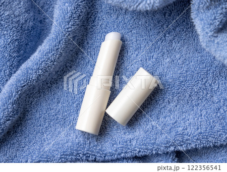 Opened white lip balm stick with a blank lid on blue bath towel top view, cosmetic mockup 122356541
