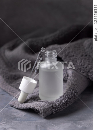 Pipette set on opened clear glass dropper bottle near dark grey bath towel closeup, cosmetic mockup 122356553
