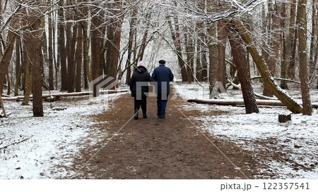 Mature couple going on snowy path at winter pine forest. Senior husband and wife walking through trail at coniferous woodland. Older pair of pensioners spending time together at nature Mature couple going on snowy path at winter pine forest. Senior husband and wife walking through trail at coniferous woodland. Older pair of pensioners spending time together at nature 122357541