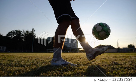 Legs of young man kicking ball at green field. Male feet of professional footballer juggling soccer ball on stadium at sunset. Sportsman practicing tricks outdoor. Concept of a freestyle football Legs of young man kicking ball at green field. Male feet of professional footballer juggling soccer ball on stadium at sunset. Sportsman practicing tricks outdoor. Concept of a freestyle football 122357554