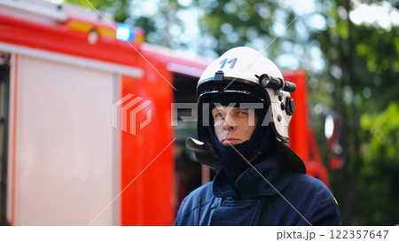 Portrait of confident male fireguard with dirty face standing near a fire engine. Young fireman in full equipment posing after fire against the background of big red truck. Concept of saving lives Portrait of confident male fireguard with dirty face standing near a fire engine. Young fireman in full equipment posing after fire against the background of big red truck. Concept of saving lives 122357647