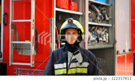 Portrait of confident female firefighter against the background of big red truck. Young firewoman in protective uniform looking at camera near a fire engine. Saving lives and heroic profession concept 122357651