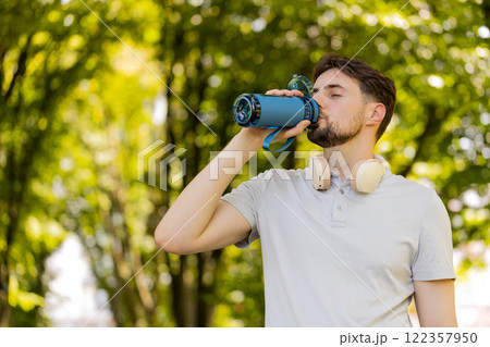 Sporty athletic thirsty man runner jogger drinking water after sport workout in park outdoors Sporty athletic thirsty man runner jogger drinking water after sport workout in park outdoors 122357950
