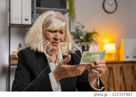 Elderly businesswoman in suit counting cash banknotes insufficient amount of money at home office Elderly businesswoman in suit counting cash banknotes insufficient amount of money at home office 122357981