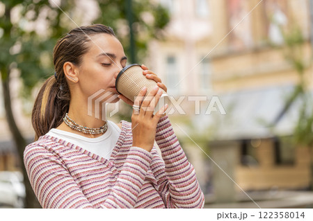 Happy smiling woman walking on city street enjoying morning coffee hot drink relaxing taking a break 122358014