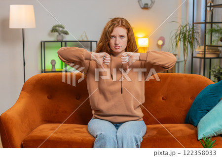 Upset woman showing thumb down sign gesture, expressing discontent sitting on sofa couch at home 122358033