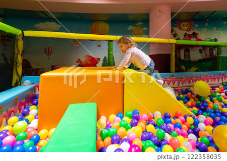 A playful child climbing a soft slide in a colorful ball pit at a vibrant indoor playground. 122358035