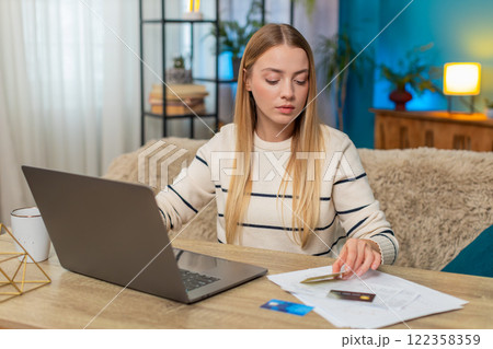 Caucasian woman checking bank account on laptop at home on table with credit cards, documents, happy Caucasian woman checking bank account on laptop at home on table with credit cards, documents, happy 122358359