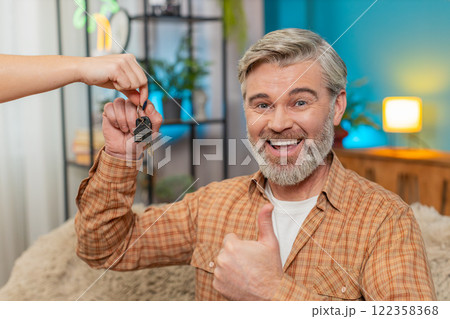 Mature man on sofa receiving keys to new apartment from realtor, smiling after lottery win at home Mature man on sofa receiving keys to new apartment from realtor, smiling after lottery win at home 122358368