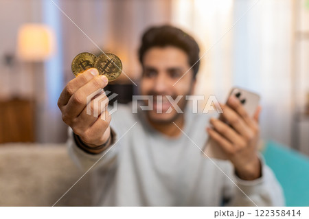 Young Indian man celebrating cryptocurrency win, showing bitcoin after checking exchange charts Young Indian man celebrating cryptocurrency win, showing bitcoin after checking exchange charts 122358414