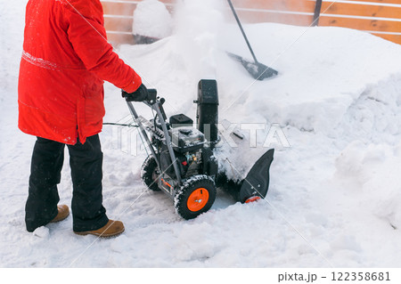 Closeup of red snow blower in action. Senior mature man outdoor in front of house using snowblower machine for removing snow on yard. Snow thrower in winter outside home. Young worker guy blowing snow Closeup of red snow blower in action. Senior mature man outdoor in front of house using snowblower machine for removing snow on yard. Snow thrower in winter outside home. Young worker guy blowing snow 122358681