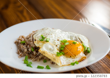 Fried eggs with boiled buckwheat and onions on a wooden table 122358783