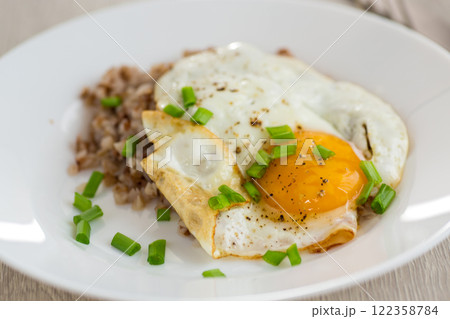 Fried eggs with boiled buckwheat and onions on a wooden table 122358784