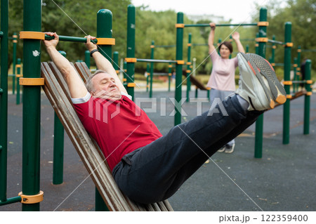 Elderly man doing exercises on a horizontal bar at an outdoor sports ground 122359400
