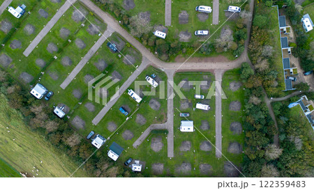 An aerial view of a campsite featuring neatly arranged pitches, caravans, motorhomes, and greenery. Pathways and surrounding trees add structure and nature to the scene. 122359483