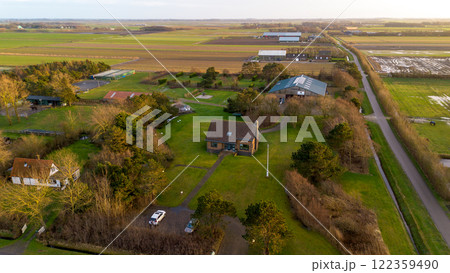 A scenic aerial view of a countryside house surrounded by lush green fields, trees, and farm buildings, with a pathway leading to the house under a partly cloudy sky. A scenic aerial view of a countryside house surrounded by lush green fields, trees, and farm buildings, with a pathway leading to the house under a partly cloudy sky. 122359490