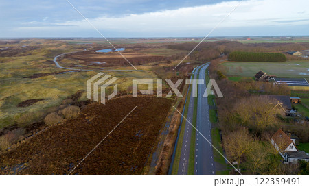Aerial view of a countryside road, bordered by fields, trees, and houses. A mix of vibrant greenery, farmland, and patches of brown vegetation creates a peaceful rural atmosphere. Aerial view of a countryside road, bordered by fields, trees, and houses. A mix of vibrant greenery, farmland, and patches of brown vegetation creates a peaceful rural atmosphere. 122359491