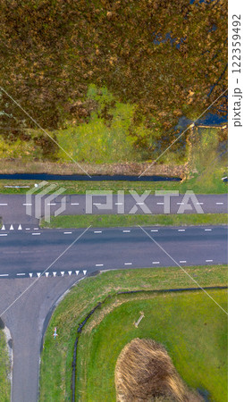 Aerial view of a rural area featuring a straight road with marked lanes, surrounded by green grass, a small canal, and patches of wetland. The vibrant landscape showcases natural and human elements. 122359492