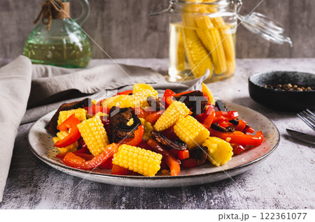 Appetizing salad of canned corn, fried mushrooms and peppers on a plate on the table 122361077