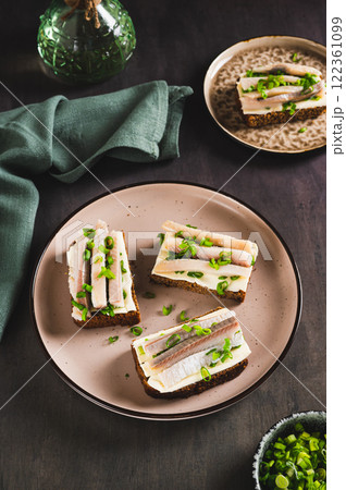 Norwegian smorrebrod made from rye bread, butter and salted herring on a plate vertical view 122361099