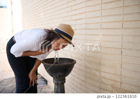 Woman drinking water from an outdoor fountain on a sunny day Woman drinking water from an outdoor fountain on a sunny day 122361810