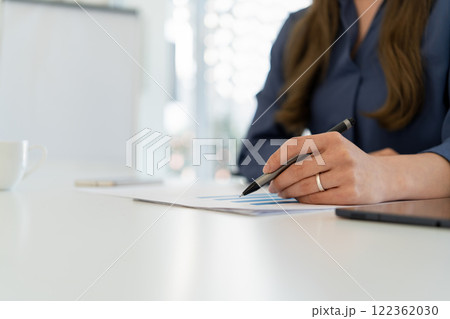 Businesswoman sitting at desk on couch in workplace or at home working on laptop and analyzing data on charts and graphs and writing on papers to make business plan and strategies for company. 122362030