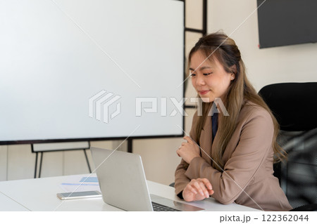 Businesswoman sitting at desk on couch in workplace or at home working on laptop and analyzing data on charts and graphs and writing on papers to make business plan and strategies for company. Businesswoman sitting at desk on couch in workplace or at home working on laptop and analyzing data on charts and graphs and writing on papers to make business plan and strategies for company. 122362044