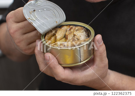 Hands open a metal fish can with sprats. Hands open a metal fish can with sprats. 122362375