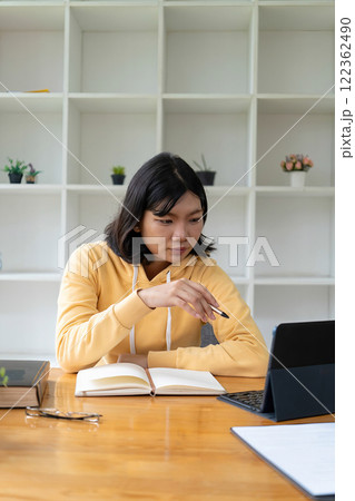 Intelligent young woman having online lessons on laptop, drinking coffee and taking notes, 122362490