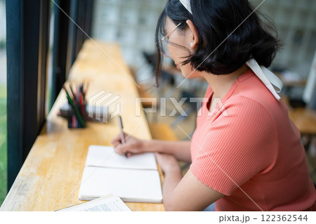Intelligent young woman having online lessons on laptop, drinking coffee and taking notes, 122362544