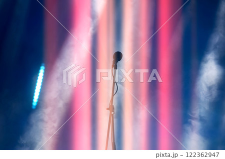A concert microphone against a background of multicolored light and smoke from the stage spotlights. 122362947