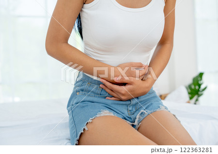 Front view and close up woman sit on bed and express of stomach ache by use two hands to hold her stomach in bedroom. 122363281