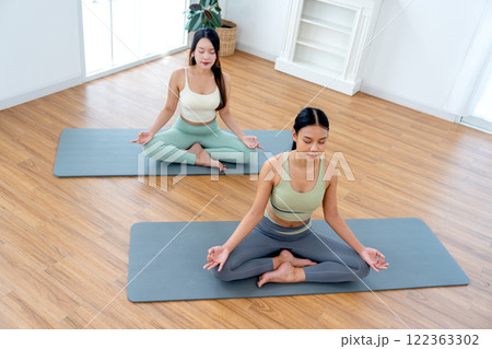 High view of two beautiful Asian women with exercise clothes do yoga posture like meditation in room with day light. 122363302