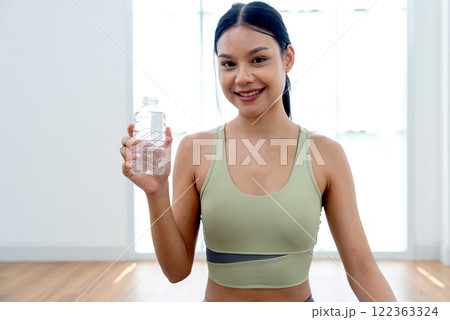 Portriat of pretty Asian woman with exercise clothes sit and hold bottle of water and look at camera with smiling during yoga exercise with happiness. Portriat of pretty Asian woman with exercise clothes sit and hold bottle of water and look at camera with smiling during yoga exercise with happiness. 122363324