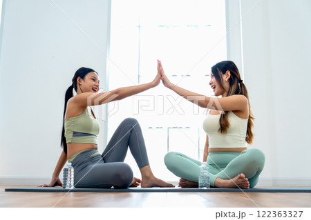 Asian women relax after yoga exercise by sit on yoga mat and touch their hands together in the room with day light. 122363327
